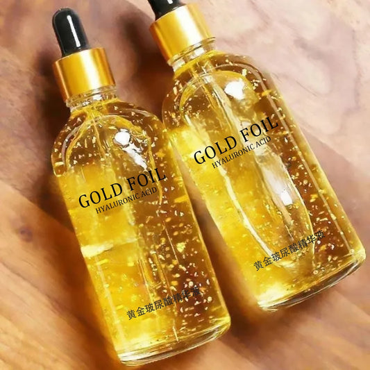 Two bottles of Gold Foil Hyaluronic Acid serum on a wooden surface.