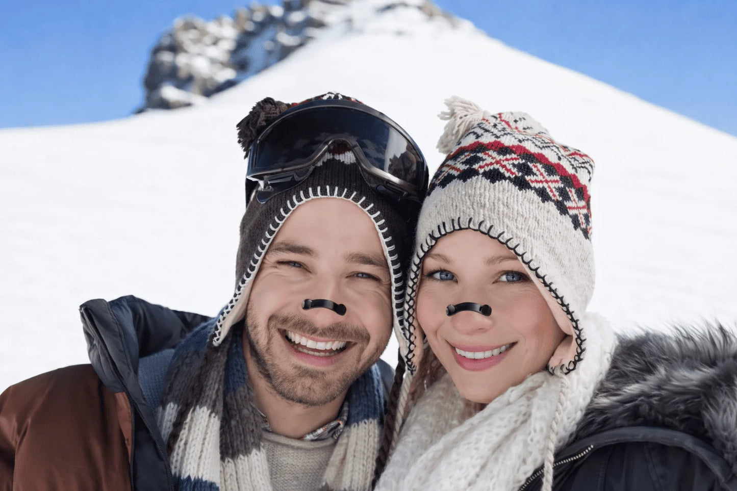 Two people in winter clothing with snow-covered mountains in the background