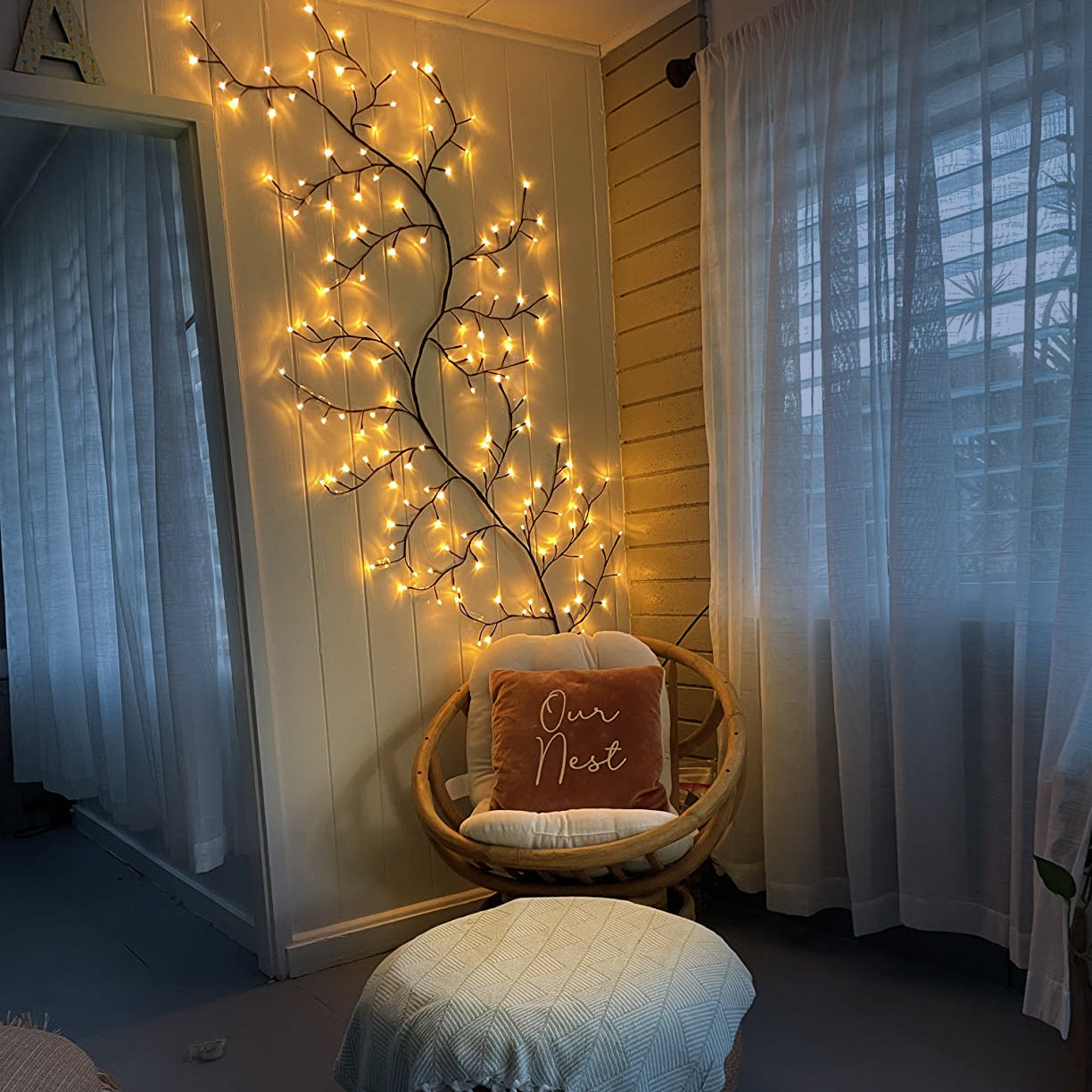 Decorative setup with a lit branch, wicker chair, and ottoman in a room.