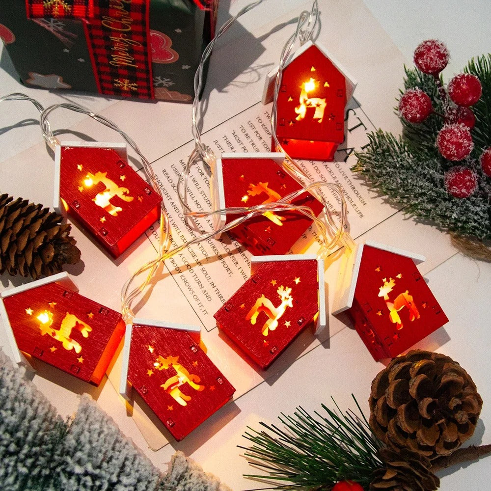 String of red house-shaped lights with gold reindeer on a festive background with pine cones and evergreen branches.