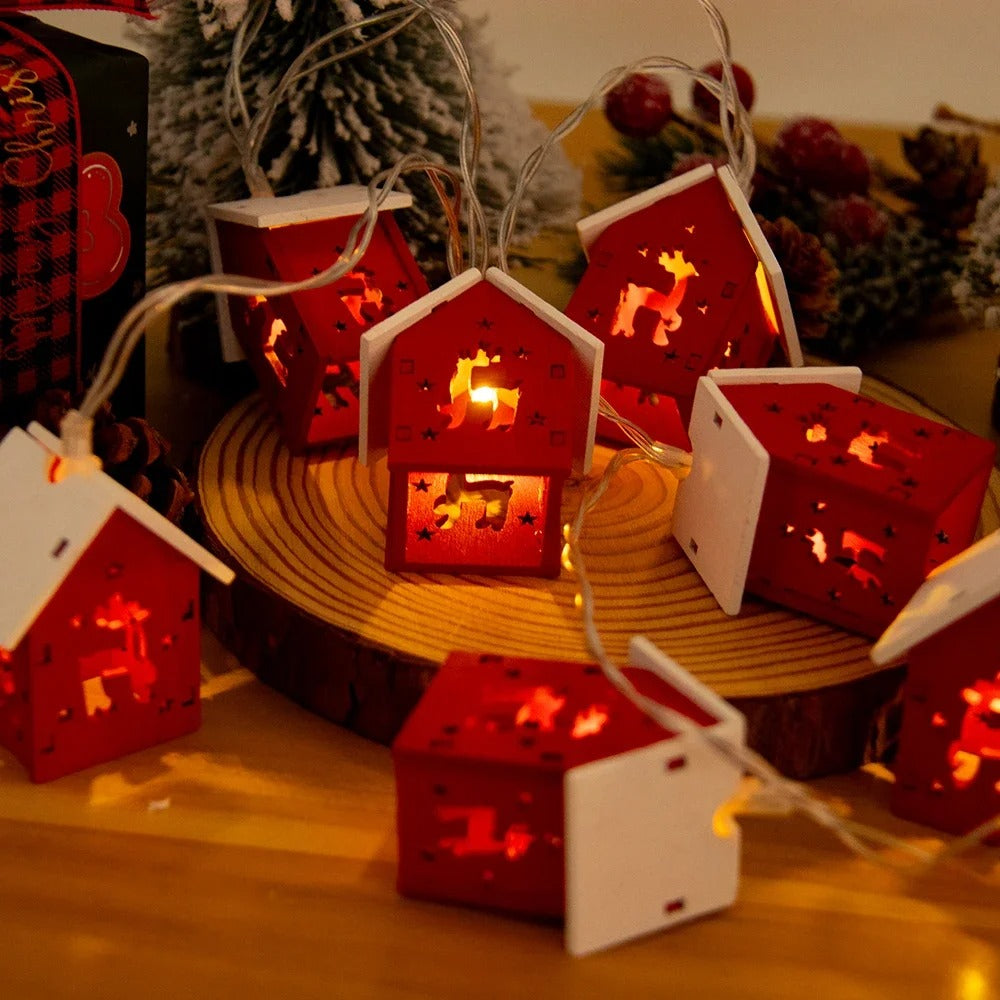 Decorative string lights shaped like red houses with white roofs on a wooden surface.