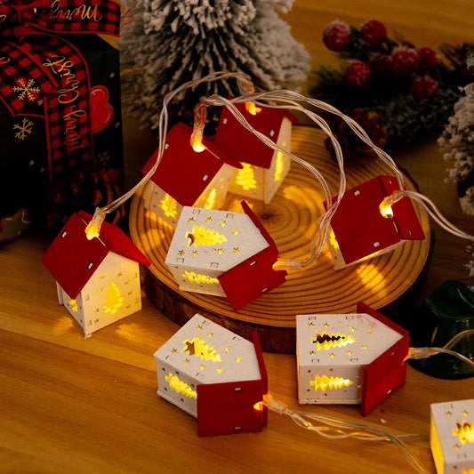 Decorative string lights shaped like small houses on a wooden surface with Christmas-themed decorations.